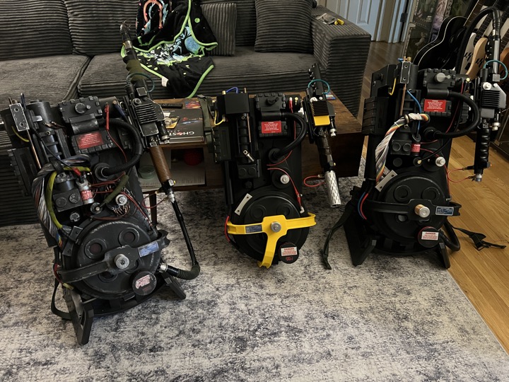 Three proton packs displayed together, with D.C.’s yellow-accented build in the center.