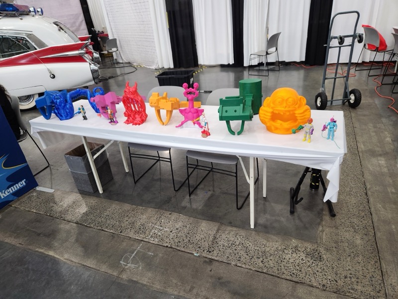 Colorful oversized props displayed alongside small Ghostbusters figures on a convention table.