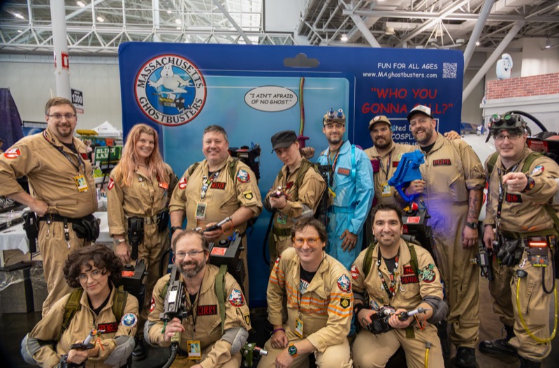 Massachusetts Ghostbusters group gathered in front of a toy-package-style convention backdrop.