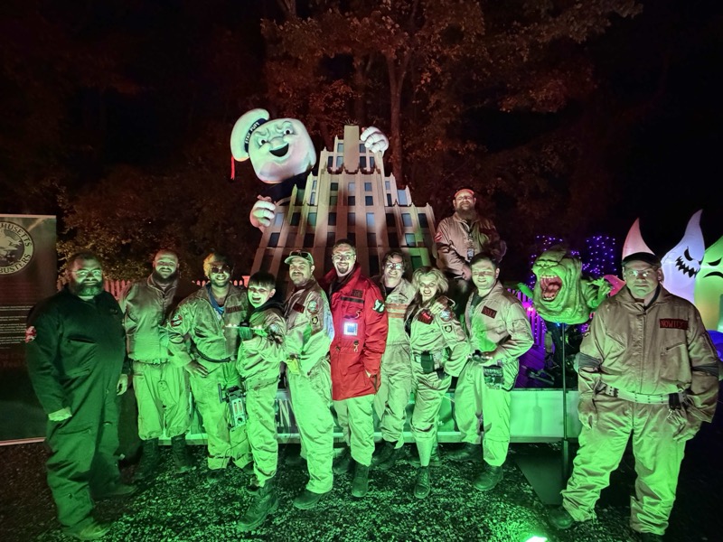 Group photo beside an illuminated Stay Puft, building display, and Slimer at an evening event.