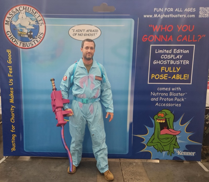Full-length view of a blue Ghostbusters costume and pink wand at the toy-package photo backdrop.